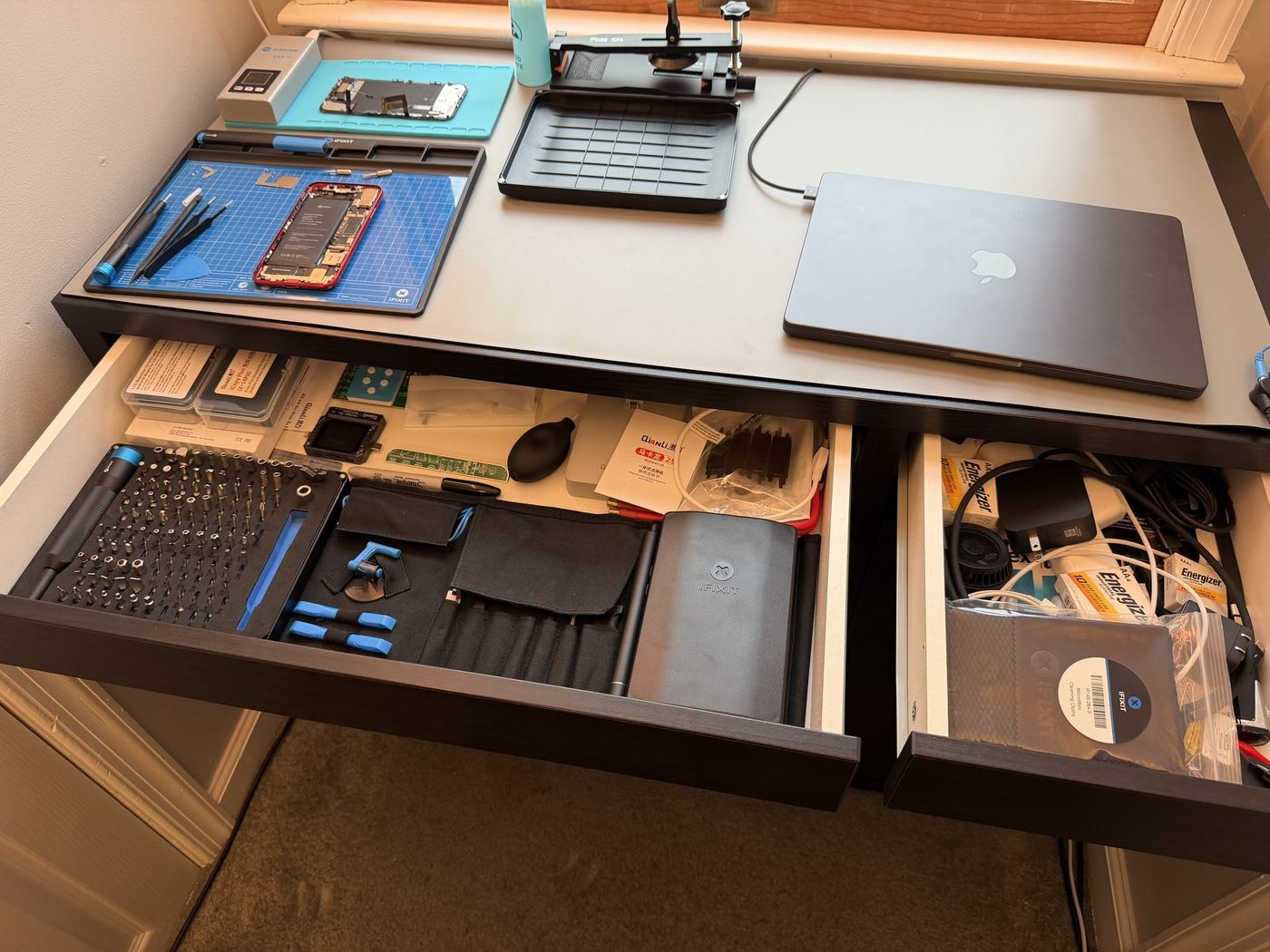 Isaac's Electronics repair bench with an iPhone mid-repair, iFixit toolkits, and a screen separator machine